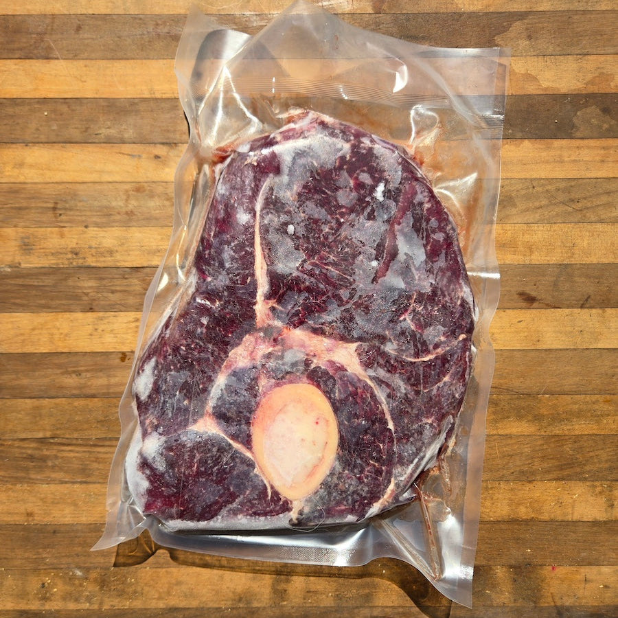 A vacuum-sealed package of beef arm roast with a bone, placed on a wooden surface