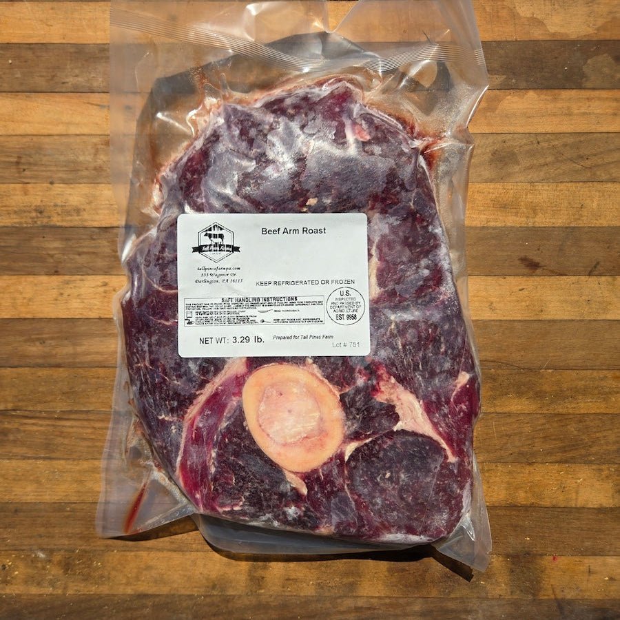 A vacuum-sealed package of beef arm roast with a bone, placed on a wooden surface