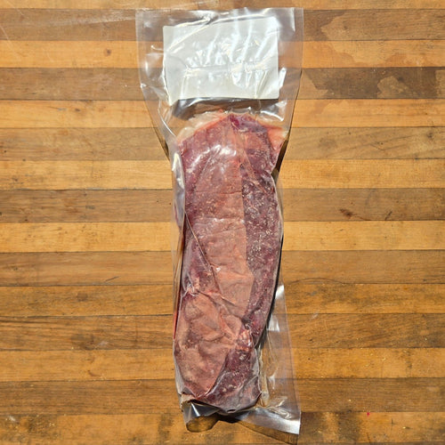 A vacuum-sealed package containing a raw cut of red meat, placed on a wooden cutting board.