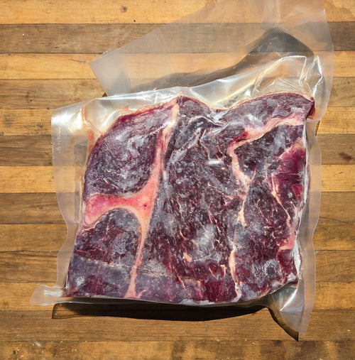 A raw marbled beef chuck roastin a clear vacuum-sealed bag placed on a wooden surface.
