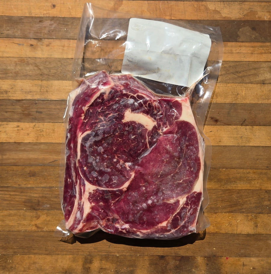 A raw beef steak in a clear plastic vacuum-sealing bag with a white paper label, placed on a wooden cutting board.