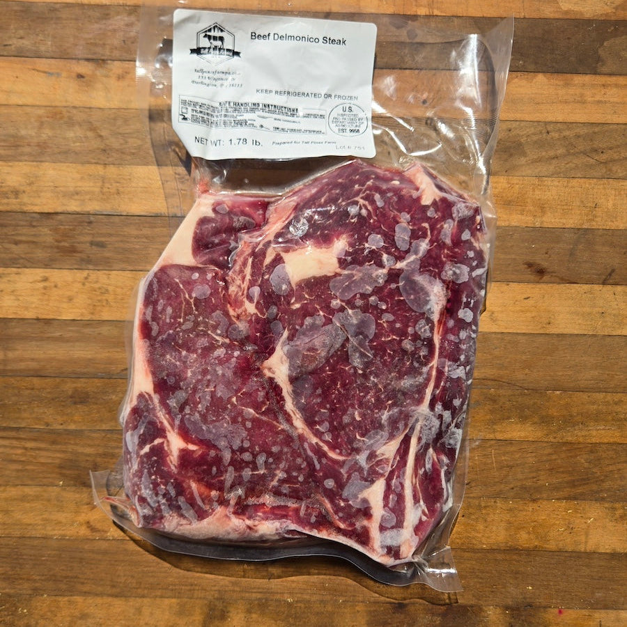A vacuum-sealed package of beef delmonico steak placed on a wooden cutting board.