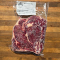 A vacuum-sealed package of beef delmonico steak placed on a wooden cutting board.