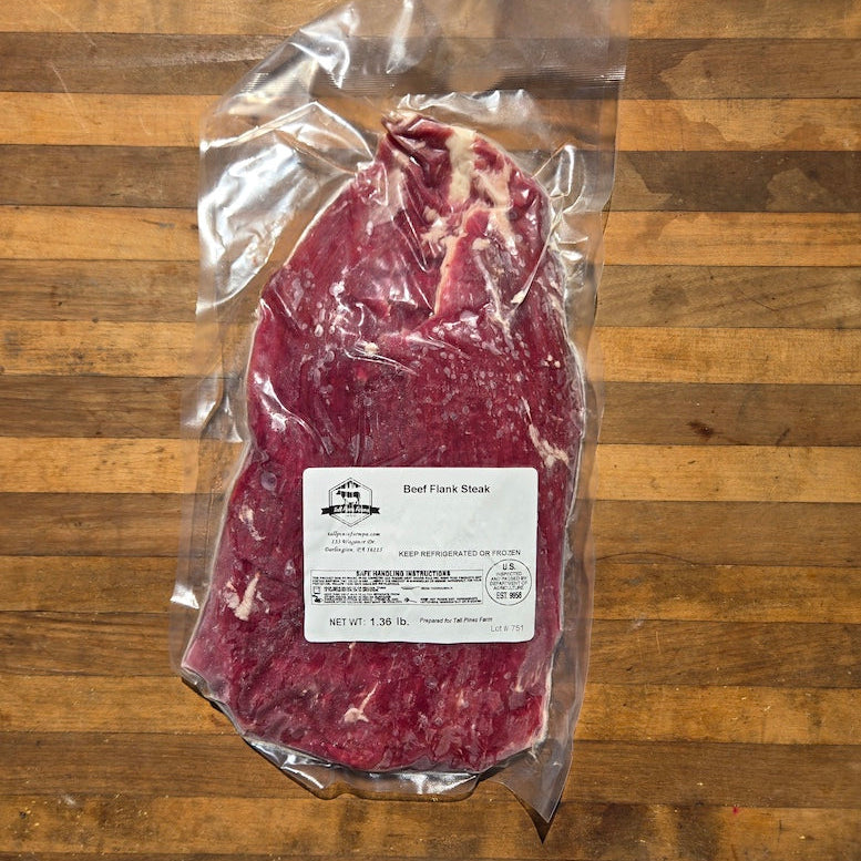 A vacuum-sealed beef flank steak with a white product label sits on a wooden surface.