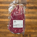 A vacuum-sealed beef flank steak with a white product label sits on a wooden surface.