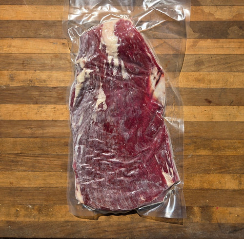 A vacuum-sealed beef flank steak sits on a wooden surface.