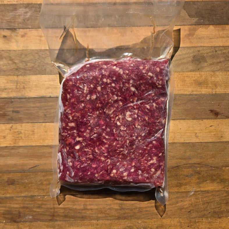 A vacuum-sealed package of ground meat placed on a wooden surface. 
