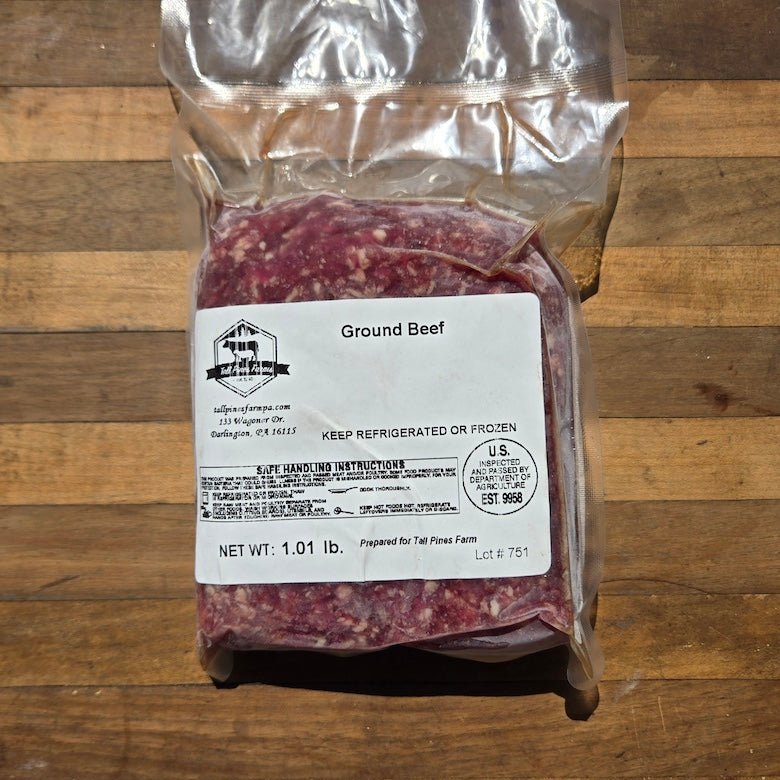 A vacuum-sealed package of ground beef with a white label, placed on a wooden surface. 