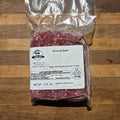 A vacuum-sealed package of ground beef with a white label, placed on a wooden surface. 