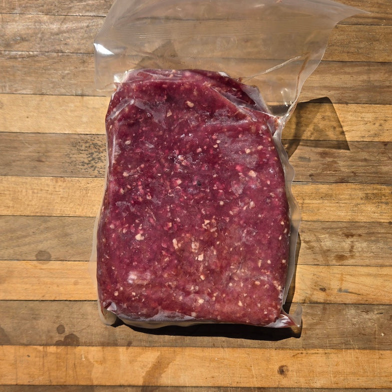 A vacuum-sealed package of ground lamb meat with a white label, sitting in a wooden surface.