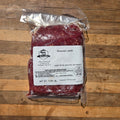 A vacuum-sealed package of ground lamb meat with a white label, sitting in a wooden surface.