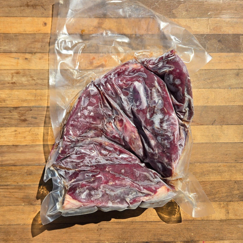 a raw, vacuum sealed beef heart. the interior is shown, displayed on a wooden surface