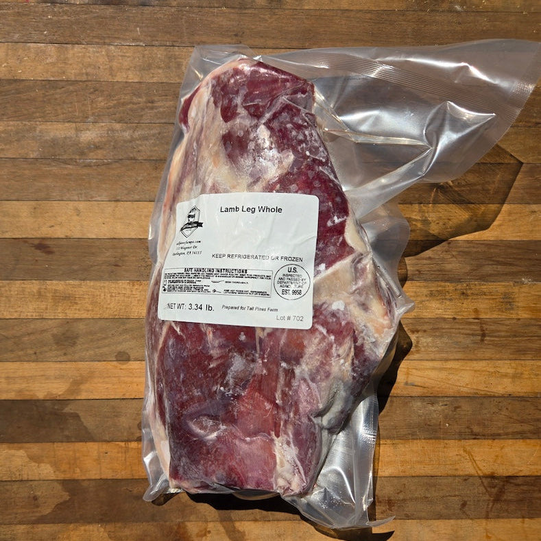 A vacuum-sealed whole lamb leg cut of meat with a white product label, placed on a wooden surface