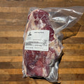 A vacuum-sealed whole lamb leg cut of meat with a white product label, placed on a wooden surface