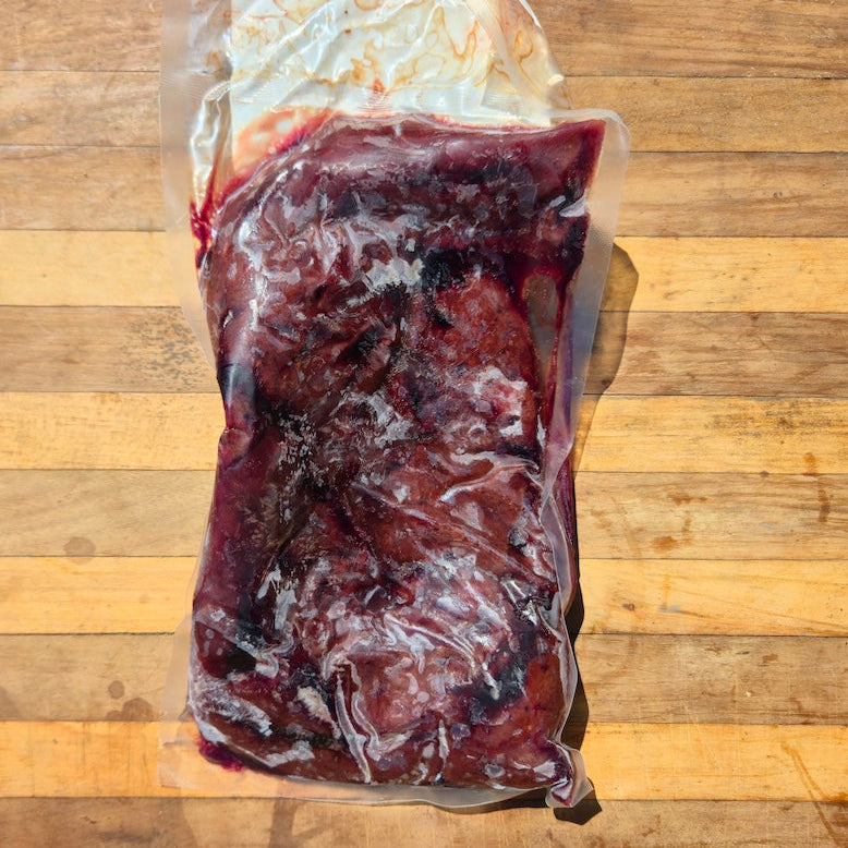 A vacuum-sealed package of raw beef liver, resting on a wooden cutting board.