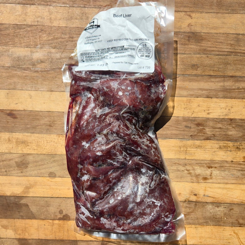 Frozen beef liver in a clear vacuum-sealed bag with a white label, placed on a wooden cutting board.