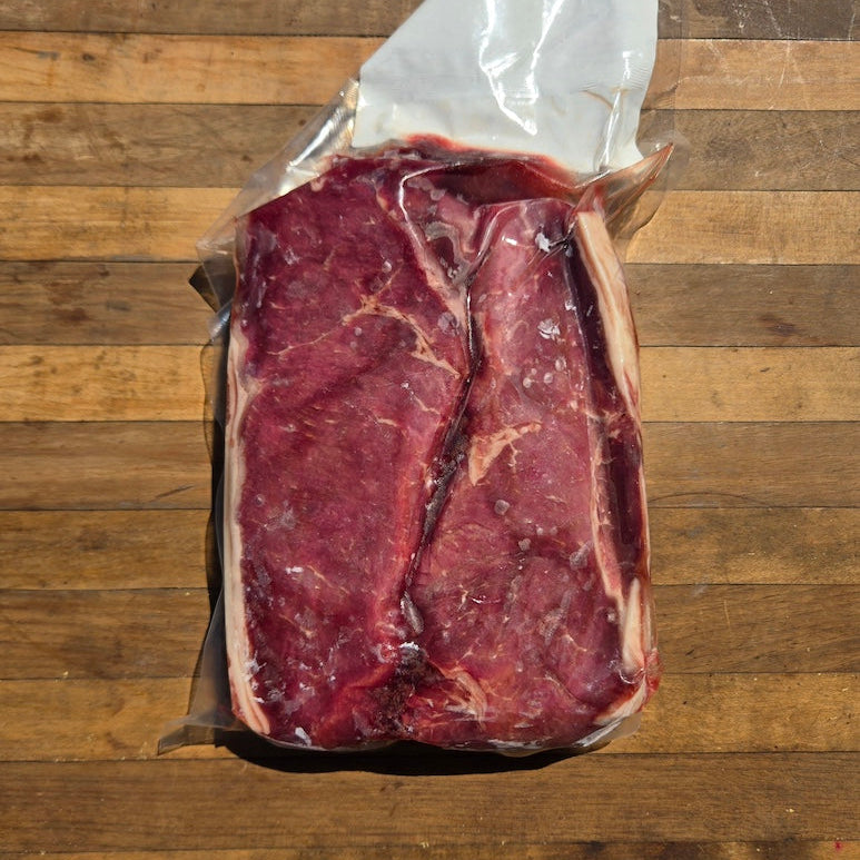 Raw vacuum-sealed beef strip steak with visible marbling, placed on a wooden cutting board.