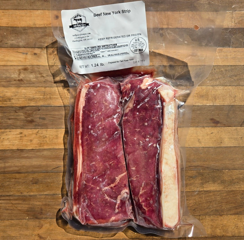 A vacuum-sealed package of beef New York strip steak on a wooden surface, with a white label at the top