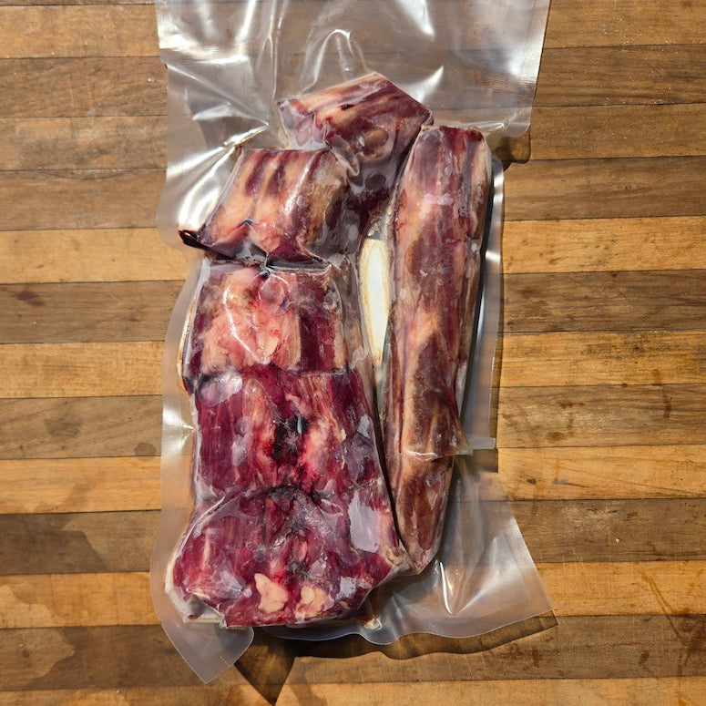 raw beef tail bones in a vacuum sealed plastic bag, displayed on a rustic wooden surface
