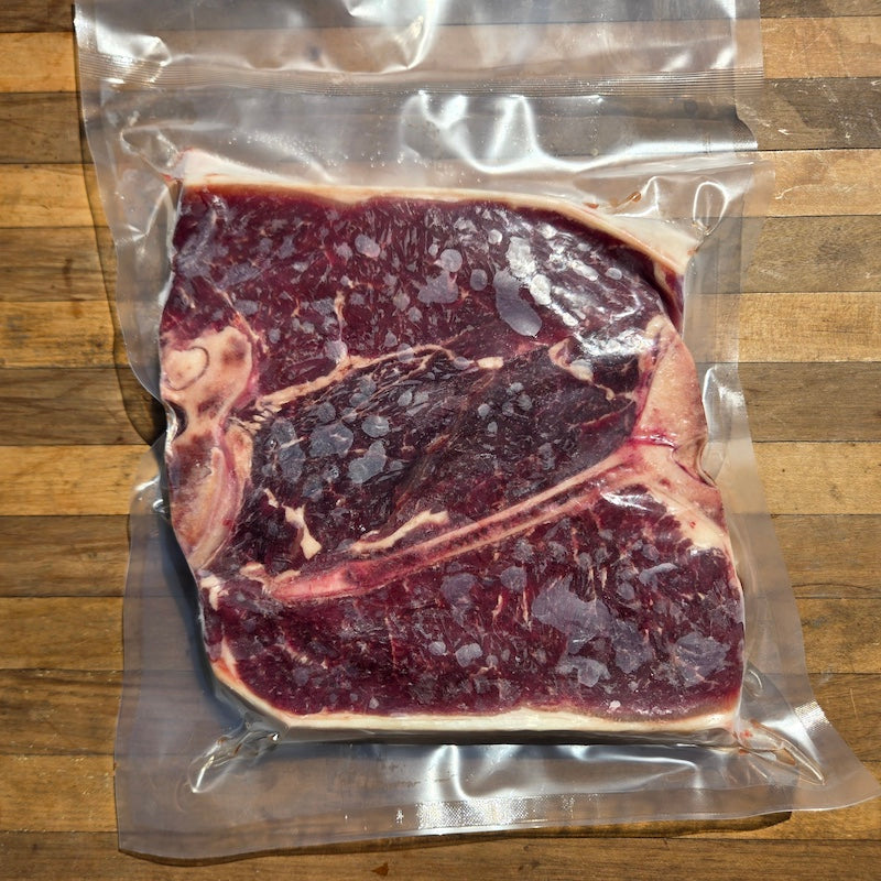 A raw porterhouse steak in a clear plastic vacuum-seal bag, placed on a wooden surface.