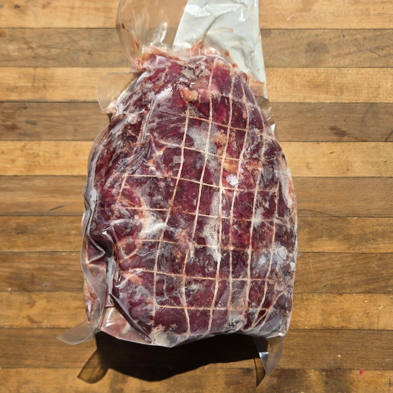 A vacuum-sealed, frozen cut of beef with a grid pattern of string, resting on a wooden surface.