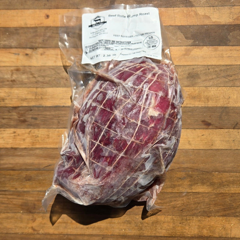 a vacuum-sealed beef rolled rump roast, with the meat in a fabric net bag, all displayed on a rustic wooden surface