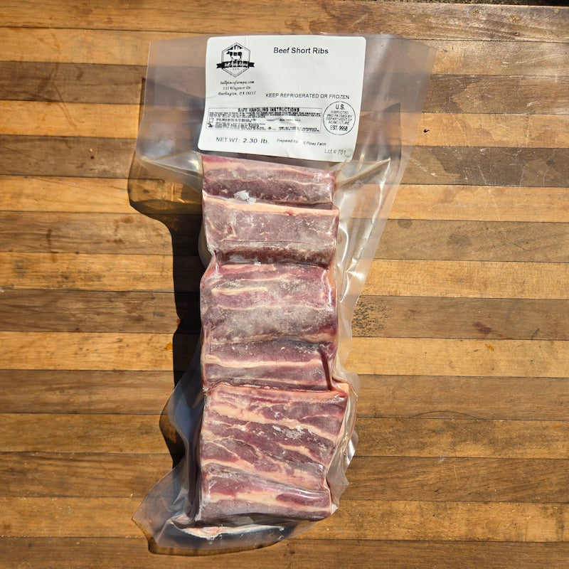 A vacuum-sealed package of beef short ribs resting on a wooden cutting board.