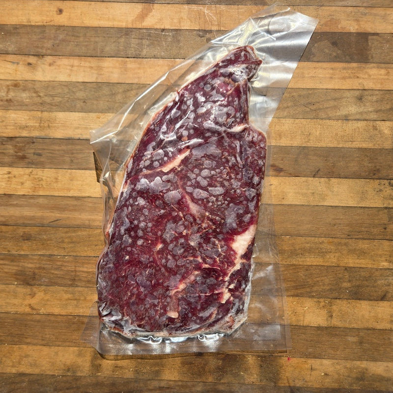 Frozen raw beef steak in clear plastic vacuum packaging, placed on a wooden surface.