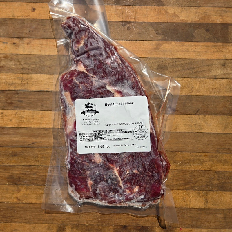 a frozen, raw sirloin steak in a vacuum-sealed package, with a white label, displayed on a rustic wooden surface