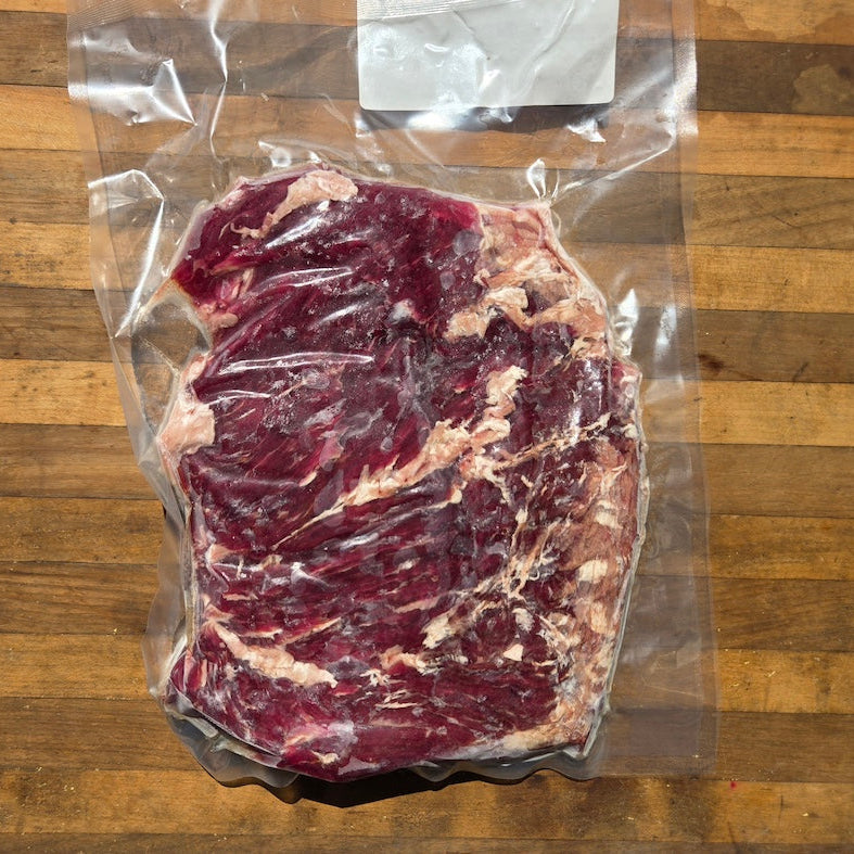 A vacuum-sealed raw cut of beef with visible marbling, placed on a wooden surface.