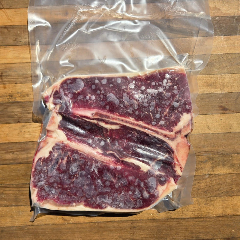 a vacuum sealed package of t-bone steaks, displayed on a wooden surface