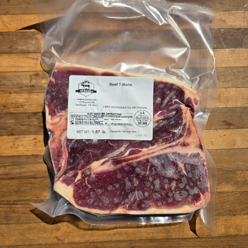 A vacuum-sealed package of beef T-bone steak on a wooden surface, with a white label showing the brand and product details.