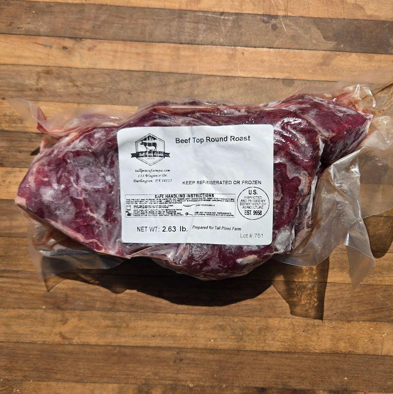 A vacuum-sealed package of beef top round roast with a white label reading 'Beef Top Round Roast' placed on a wooden surface.