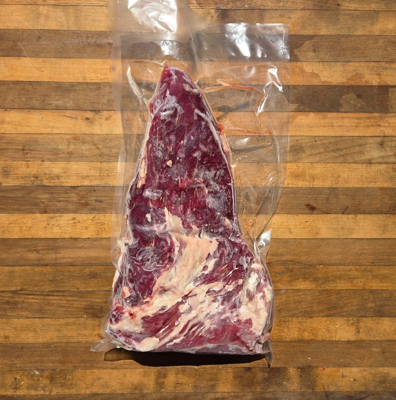 the back of a tri-tip roast in a vacuum-sealed package displayed on a wooden board