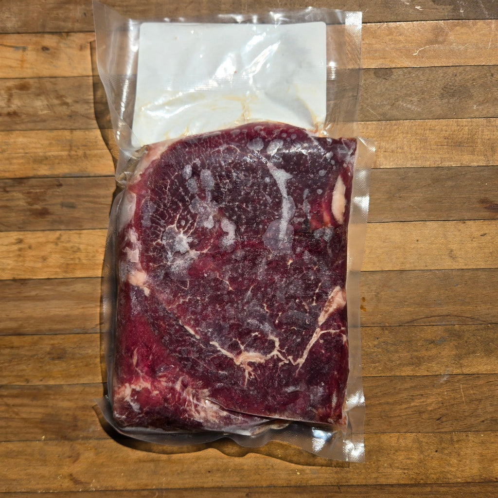 A raw, vacuum-sealed beef filet, resting on a rustic wooden surface.